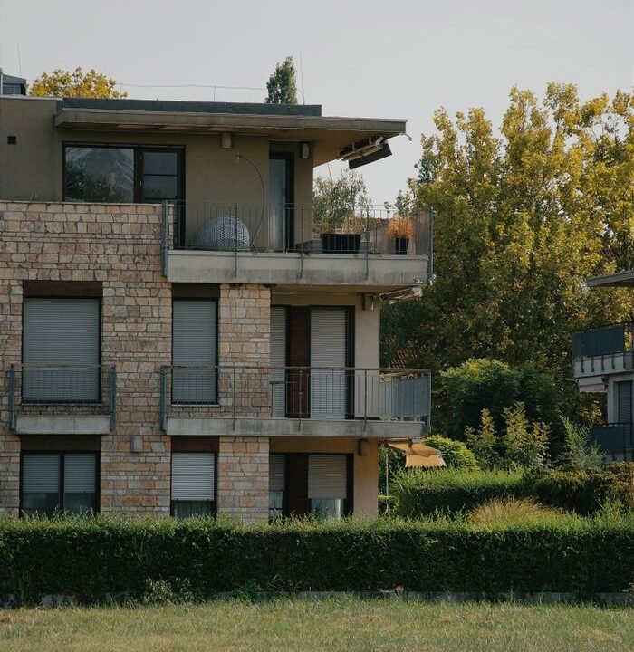 Modern Hungarian apartment building with stone facade and lush greenery on a summer day.